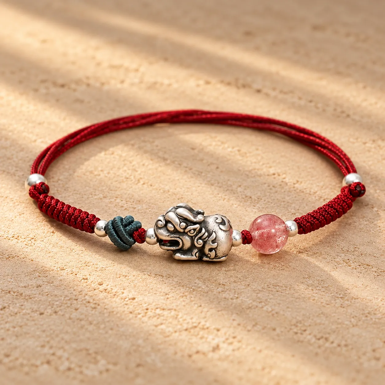 A braided red cord bracelet with a silver-plated pixiu and a pink bead