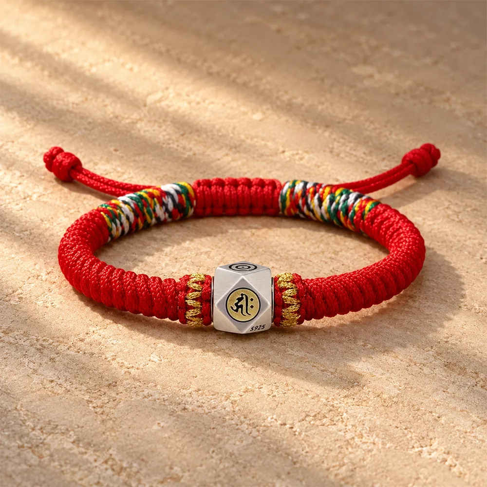 A hand-braided red cord bracelet with a silver-plated bead struck with a Sanskrit syllable