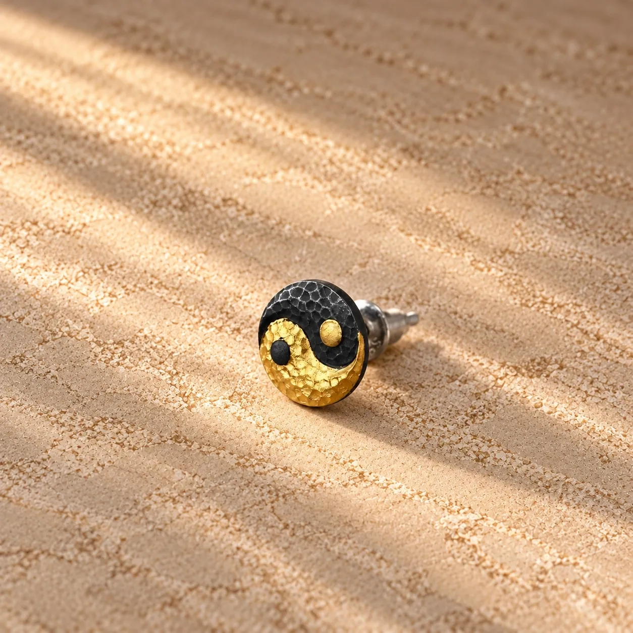 A yin-yang stud earring, gold-plated and black, resting on dark stone