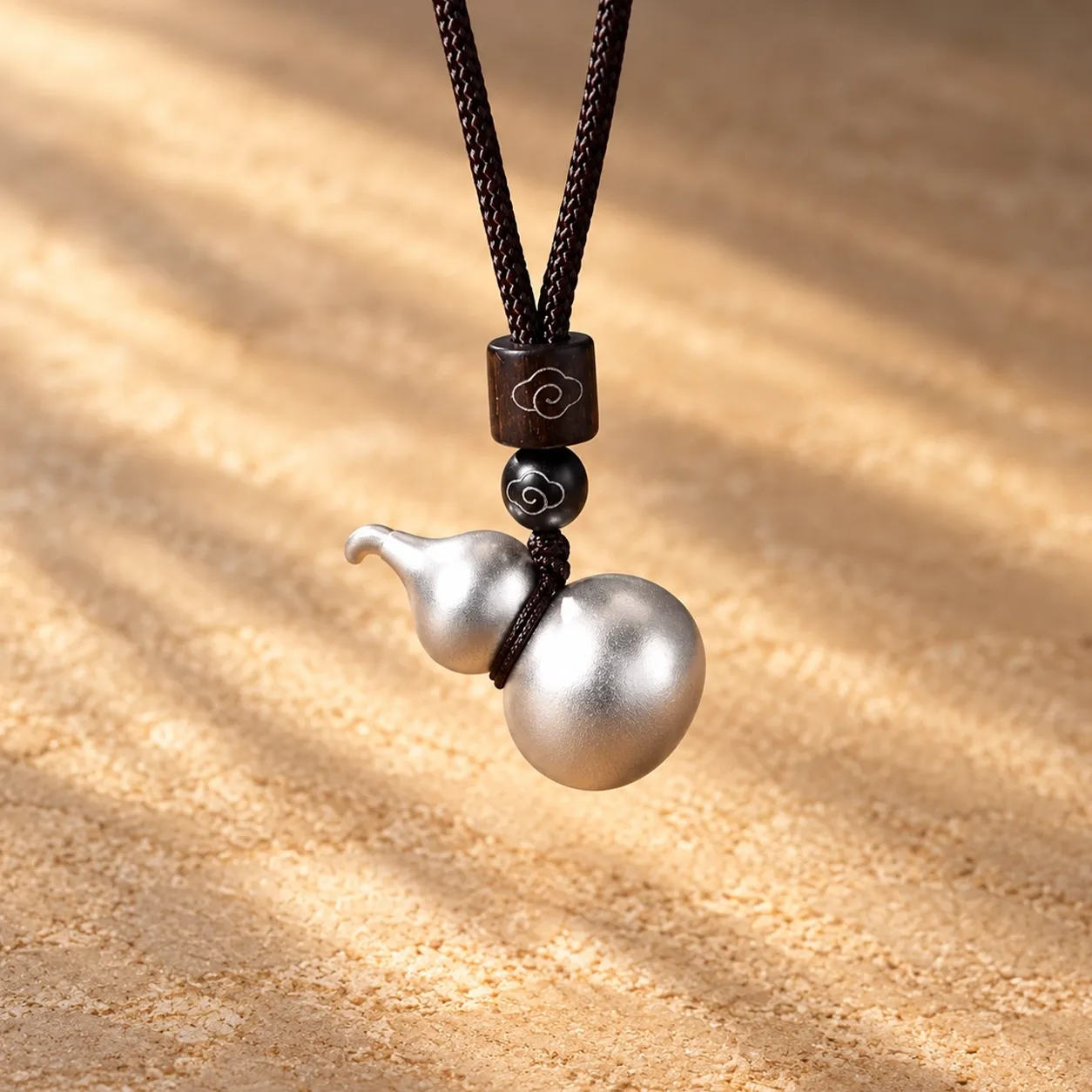 A silver-plated gourd pendant on a dark cord