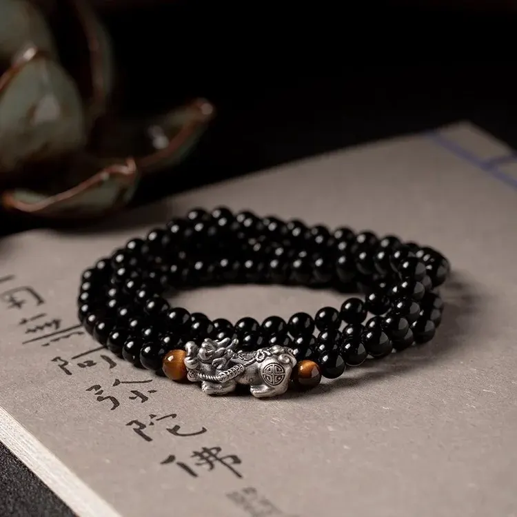 An obsidian Pixiu bracelet resting on a sutra page