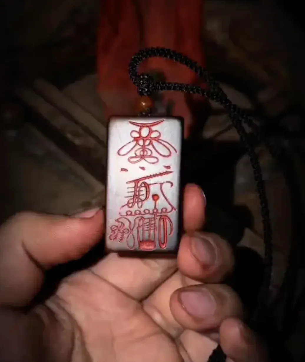 A hand holding a pale stone pendant painted with a Taoist talisman