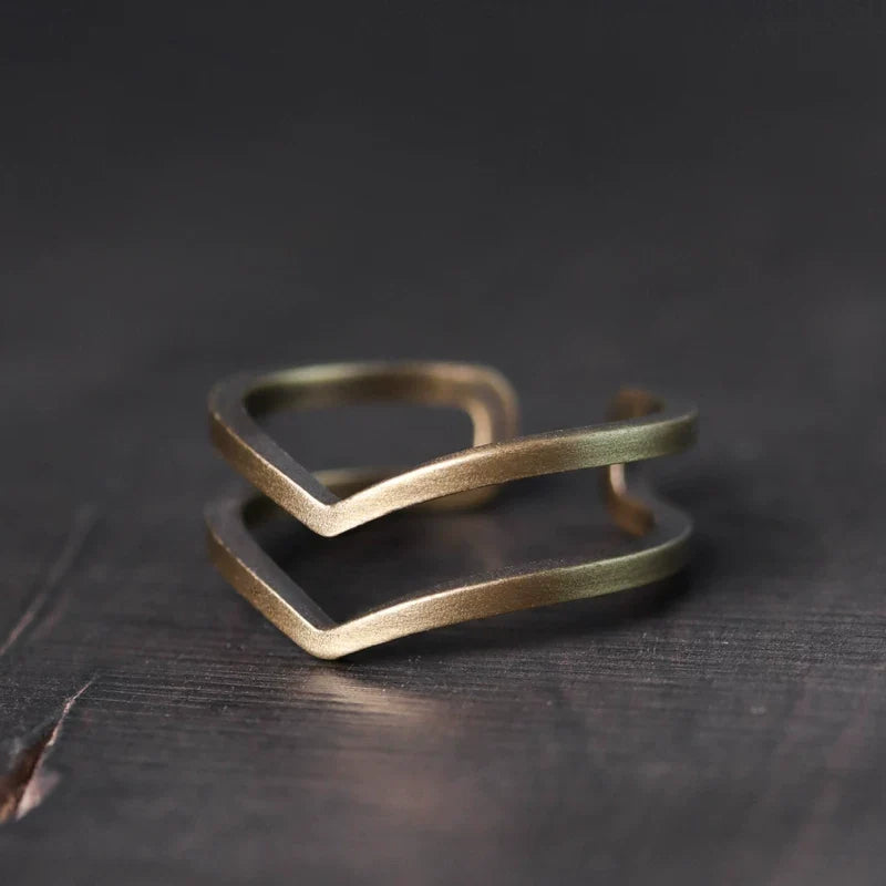 Double chevron copper ring on a dark wood surface