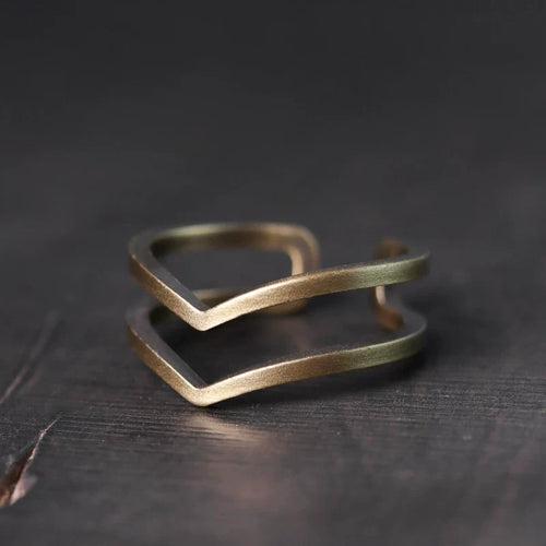 Double chevron copper ring on a dark wood surface