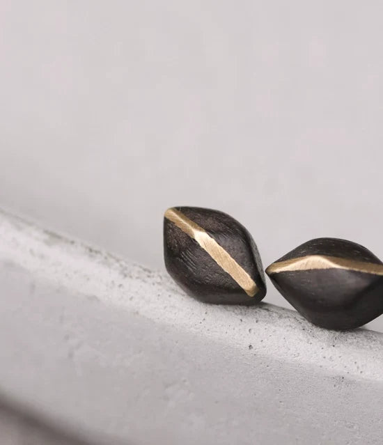 Faceted ebony stud earrings with copper inlay on a concrete ledge