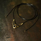 Openwork copper V pendant on a long black cord with copper bead ends on a rusted surface