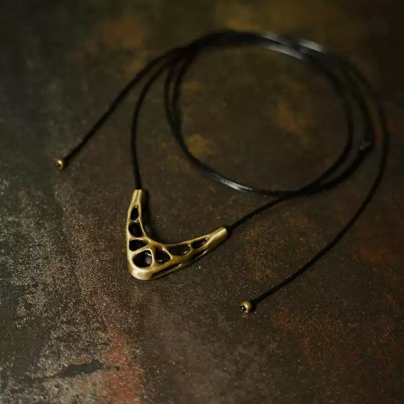 Openwork copper V pendant on a long black cord with copper bead ends on a rusted surface