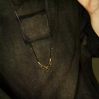 Copper V pendant on black cord worn over a dark linen shirt