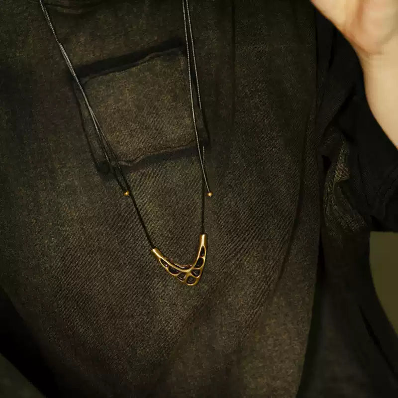 Copper V pendant on black cord worn over a dark linen shirt