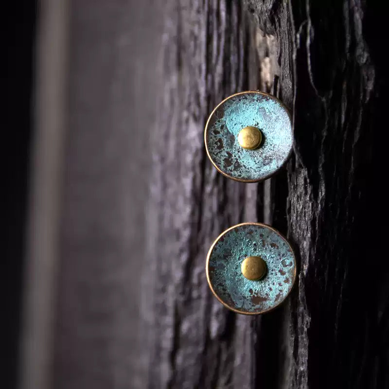 Round patina copper stud earrings displayed on dark weathered wood