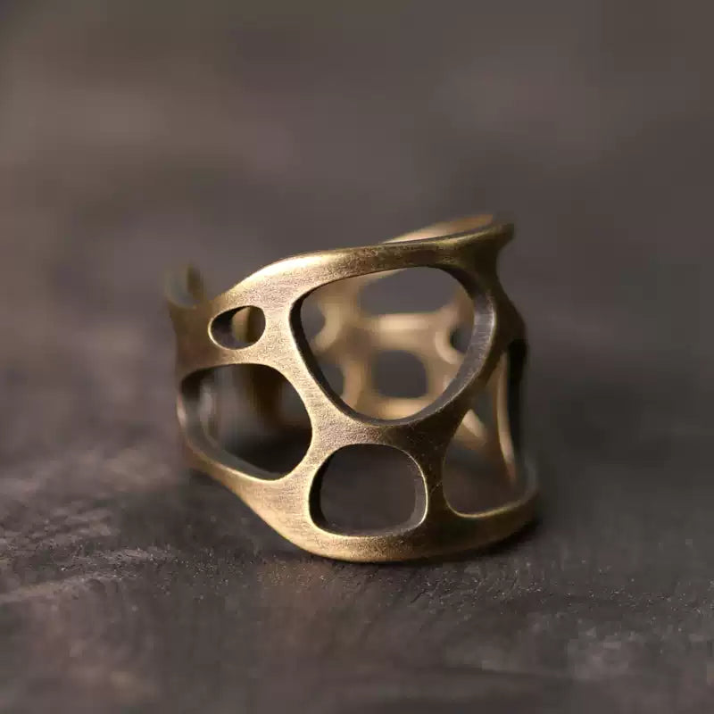 Openwork copper ring with organic cutouts on a dark wood surface