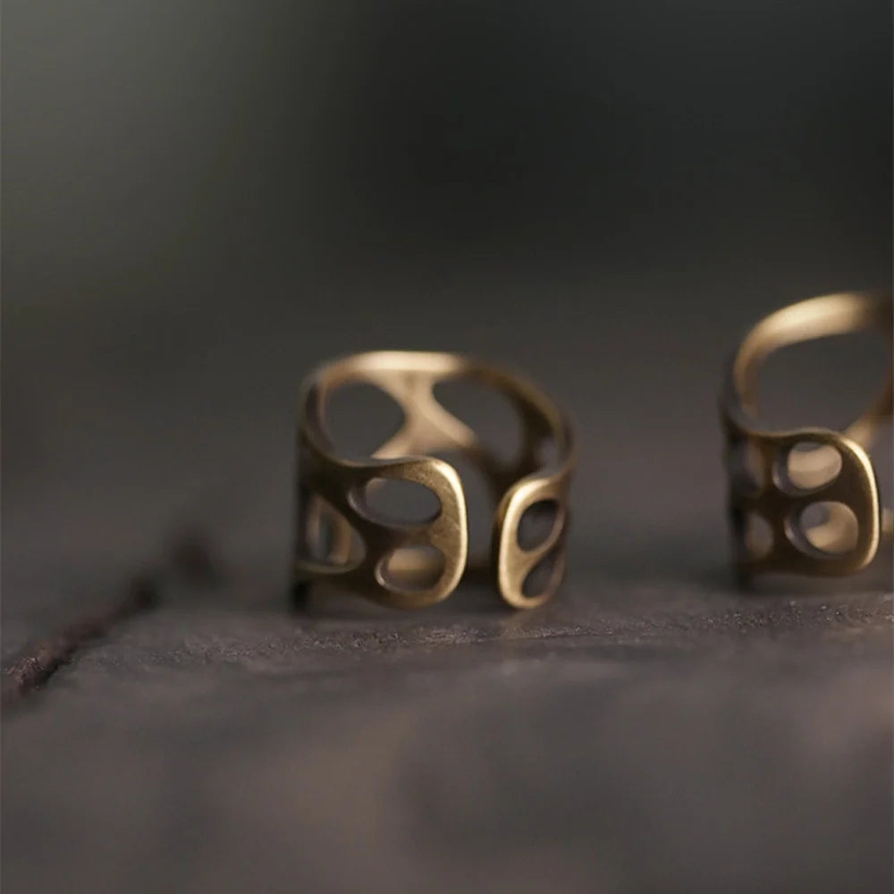 Two sculptural openwork copper rings on a dark surface