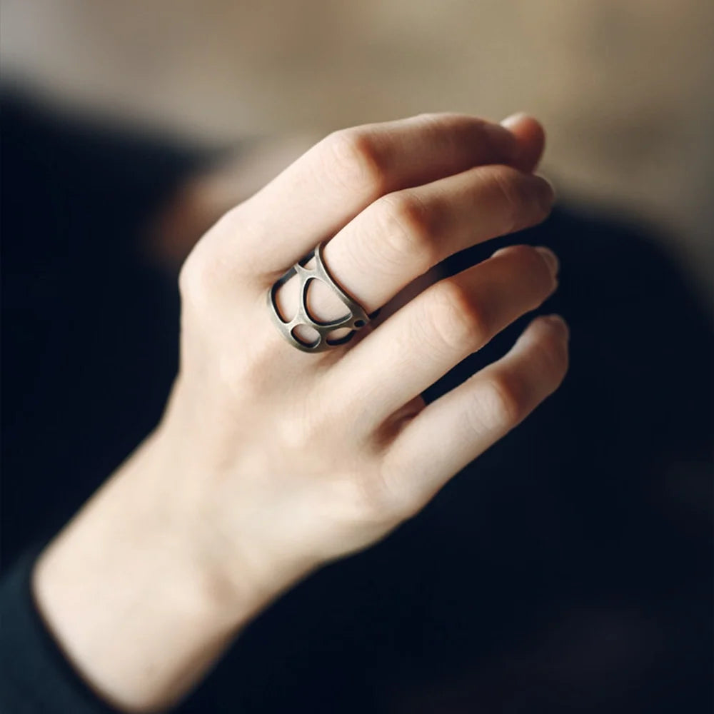 Sculptural copper ring worn on the hand against a dark background