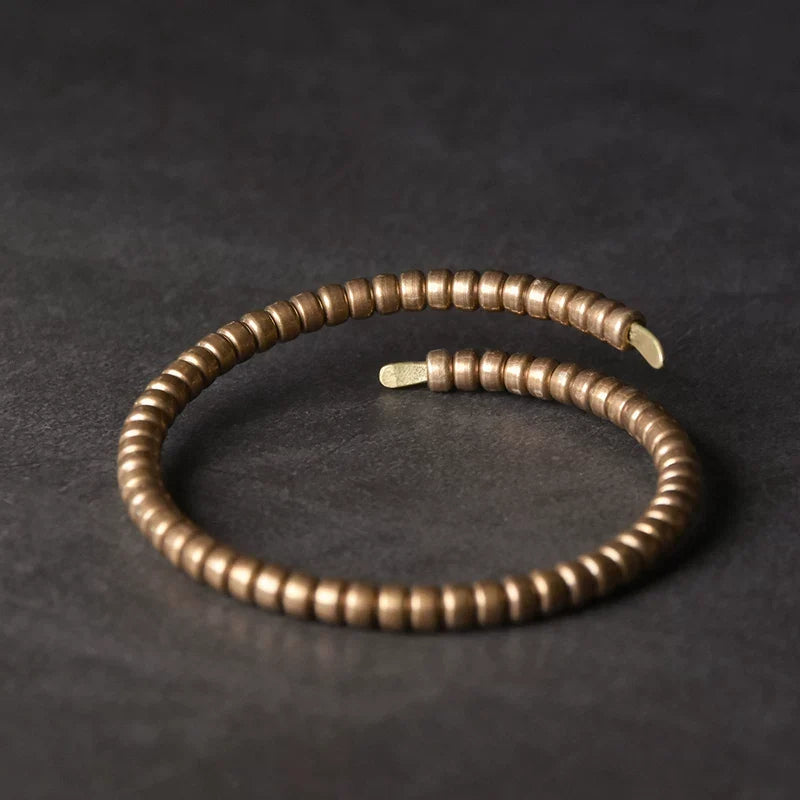 Segmented copper coil bracelet lying on a dark leather surface
