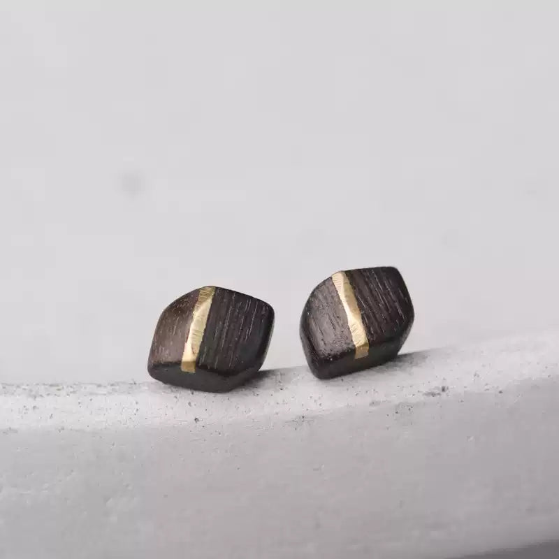 Square ebony wood studs with a copper stripe on a concrete surface