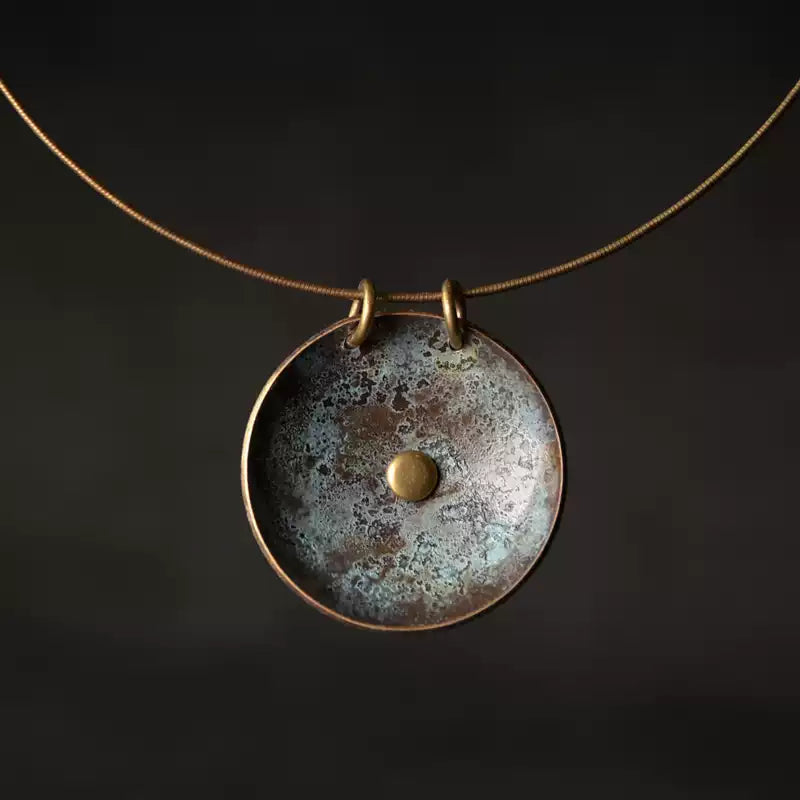 Copper disc pendant with verdigris patina and domed center on a dark background