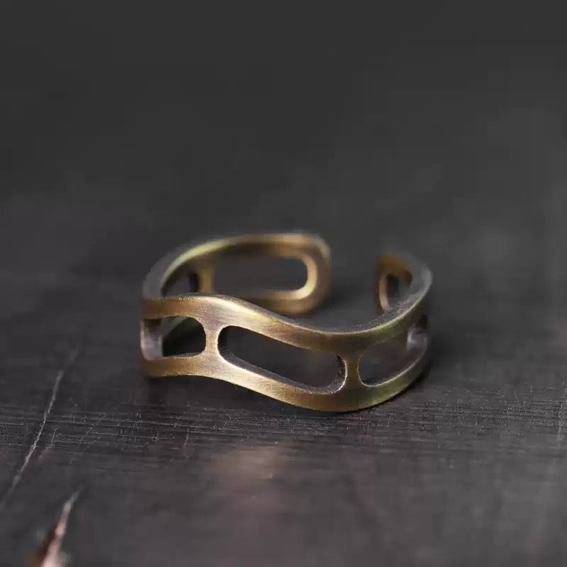 Wavy openwork copper ring on a dark wood surface