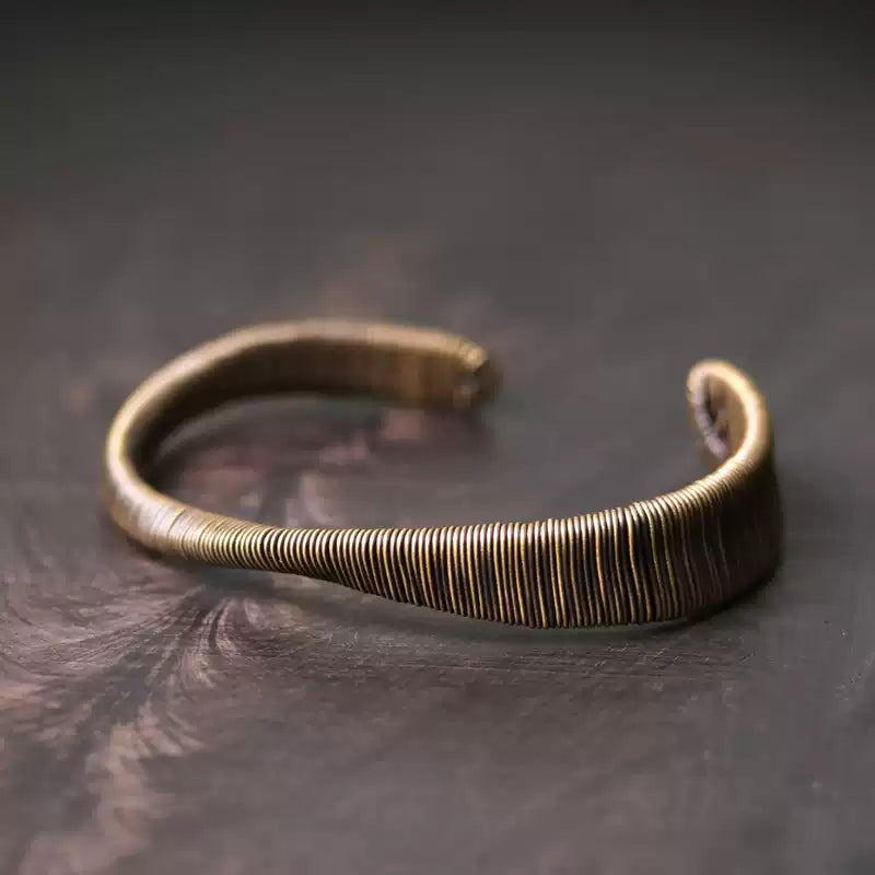 Wire-wrapped copper cuff bracelet on a dark burl wood surface