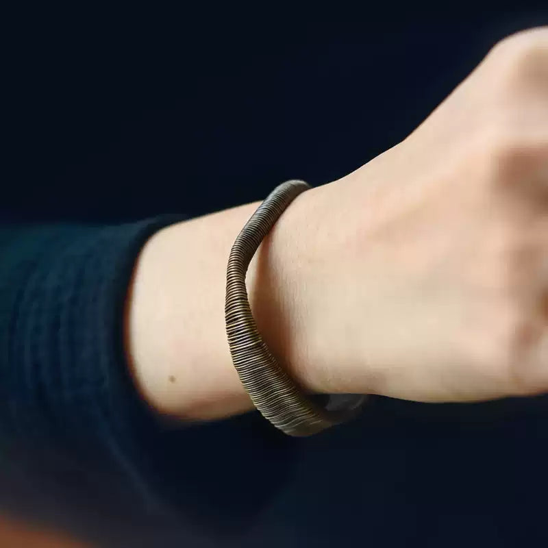 Wire-wrapped copper cuff bracelet worn on the wrist with a navy sleeve