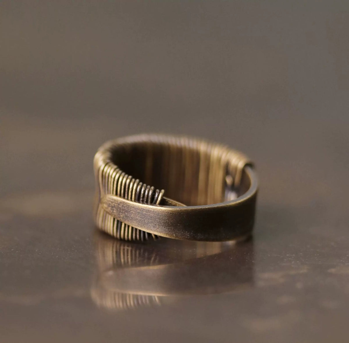 Wire-wrapped copper ring with its reflection on a dark glossy surface